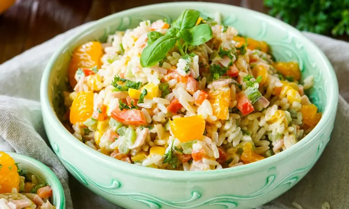 Erfrischender Reissalat mit Mandarinen, Paprika und Kräutern, garniert mit Basilikum.