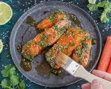 Vorbereitung für ein köstliches Gericht: Lachs marinieren mit Kräutern und Sesam. Eine Hand mit Pinsel verteilt die Marinade.