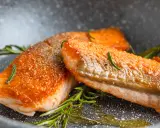 Zwei perfekt gebratene Lachsfilets mit knuspriger Haut und Rosmarin in einer Pfanne.