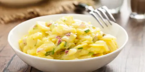 Schüssel mit cremigem Kartoffelsalat, garniert mit roten Zwiebeln und Schnittlauch. Ein köstliches Rezept für Kartoffelsalat!