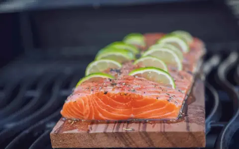 Ein saftiges Lachsfilet mit Limettenscheiben und Kräutern wird auf einem Holzbrett gegrillt.
