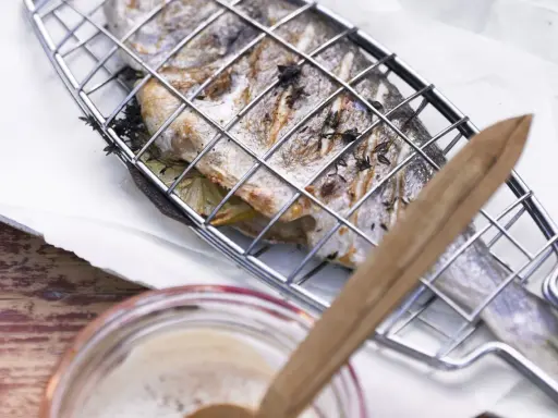 Ein ganzer Fisch liegt in einem Grillkorb, bereit zum Fisch grillen auf dem Elektrogrill. Kräuter und Zitronenscheiben sind im Fisch.