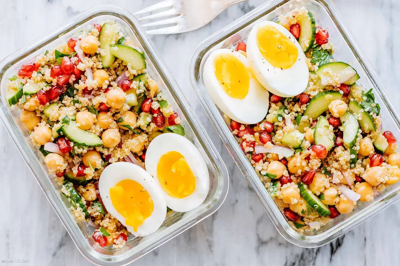 Zwei Beh&auml;lter mit Quinoa Salat, Kichererbsen, Granatapfel, Gurke und gekochten Eiern.