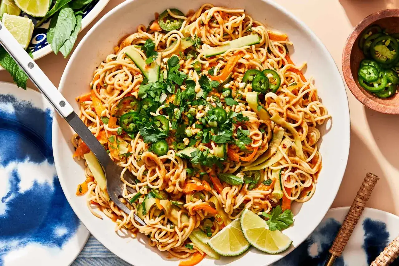 Ein k&ouml;stlicher asia nudelsalat mit Gurke, Karotten, Jalape&ntilde;os und Koriander, garniert mit Erdn&uuml;ssen und Limettenspalten.