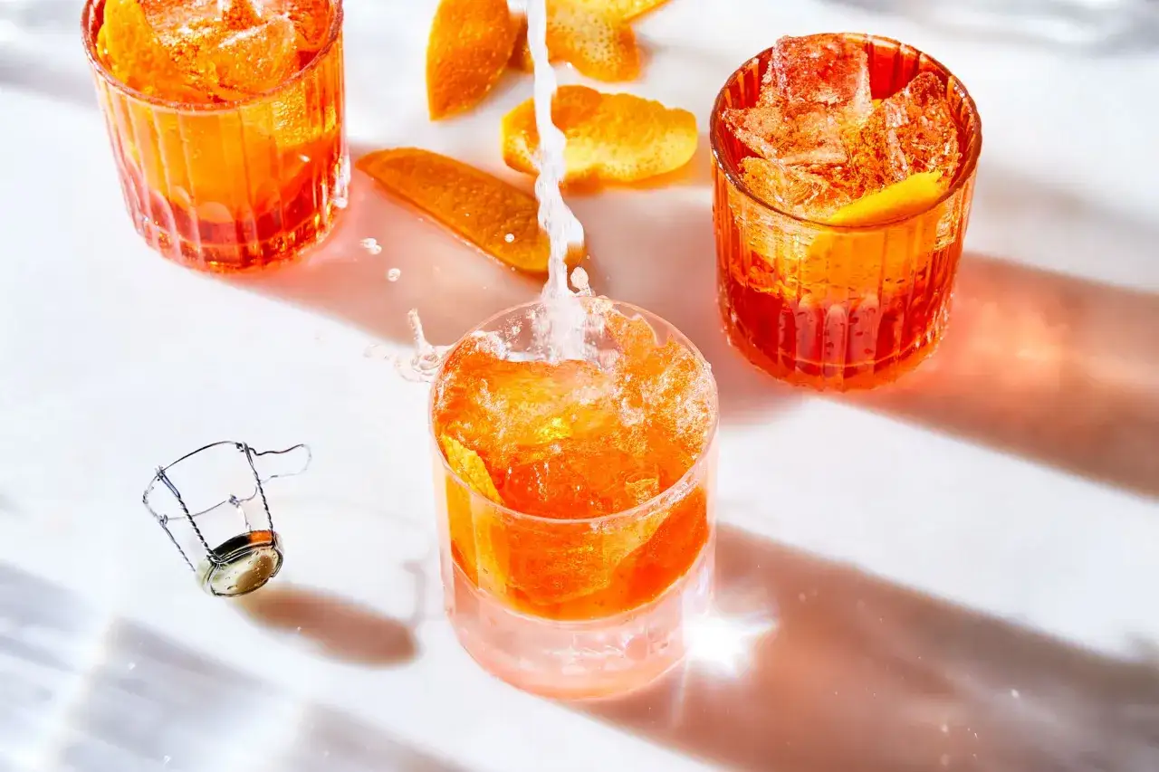 Erfrischender Cocktail mit Prosecco und Orangenzesten, Eisw&uuml;rfel sprudeln.