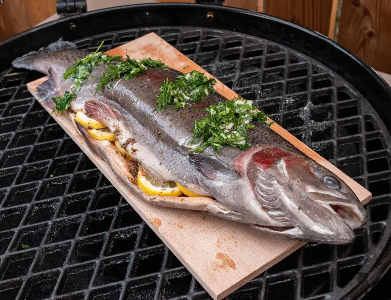 Ein ganzer Fisch mit Zitrone und Kr&auml;utern wird auf einem Holzbrett gegrillt.