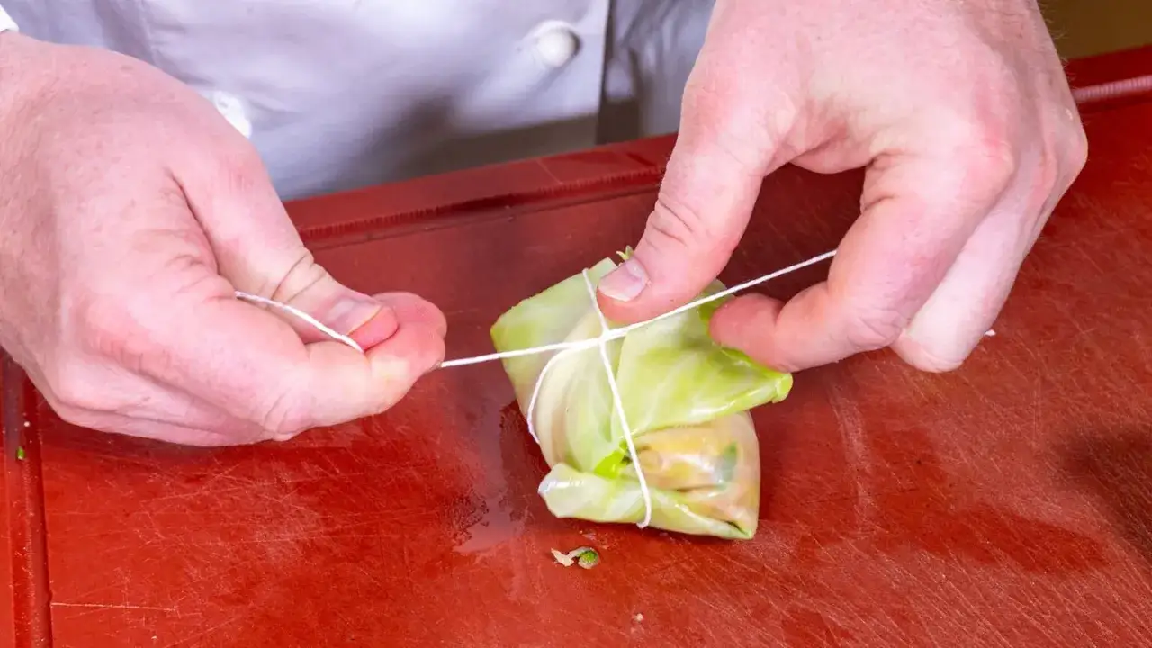 H&auml;nde binden Kohlrouladen mit Schnur. Ein Schritt im Kohlrouladen Rezept, um die F&uuml;llung sicher zu verpacken.