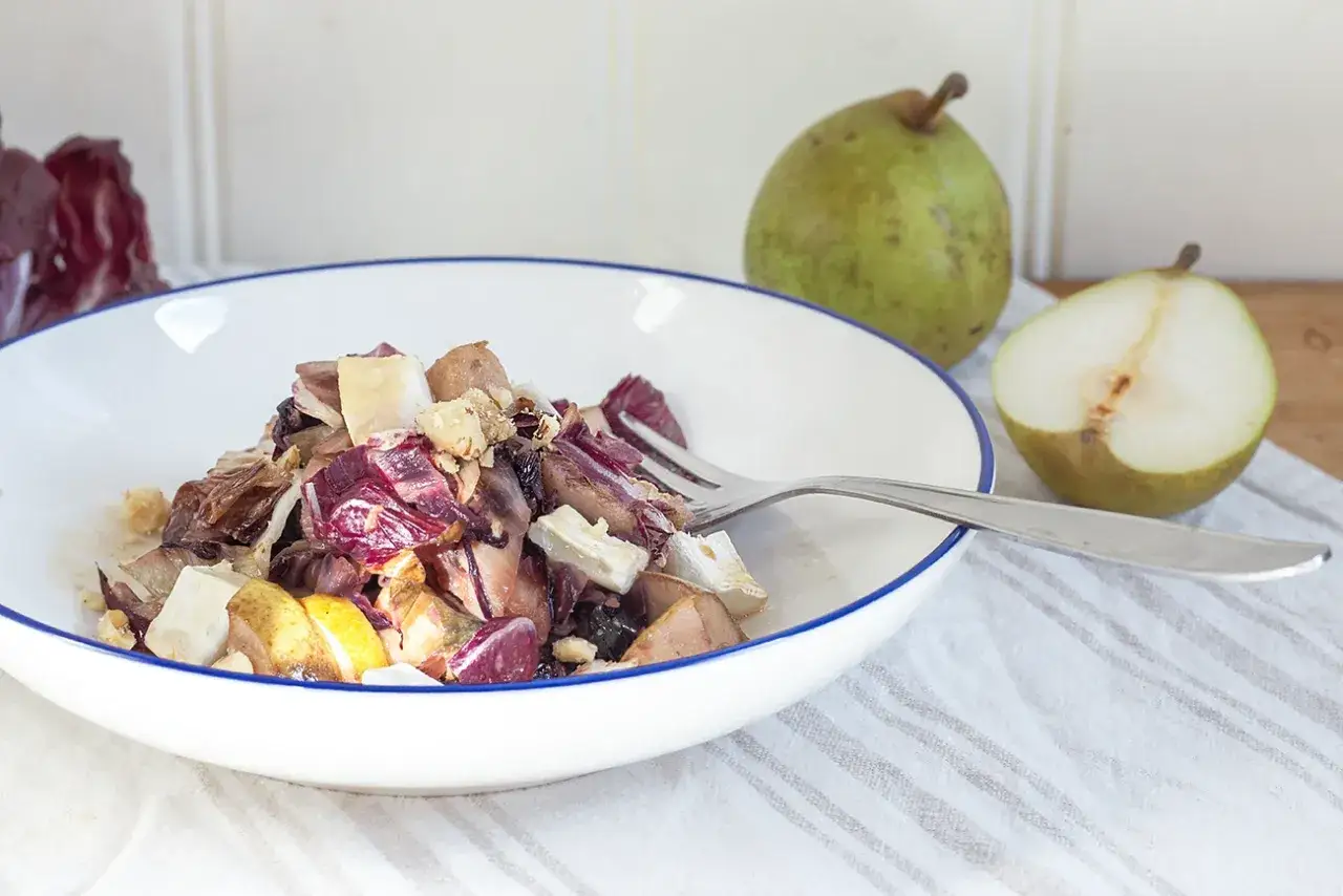 Ein k&ouml;stlicher Radicchio Salat mit Birnenst&uuml;cken und N&uuml;ssen, serviert in einer wei&szlig;en Sch&uuml;ssel mit blauem Rand.