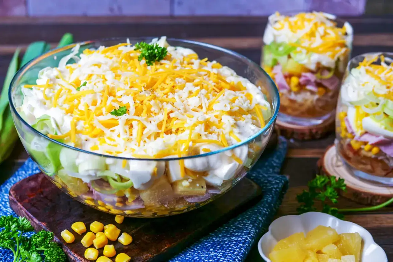 Schichtsalat rezept: Ein bunter Schichtsalat in einer Glasschüssel, garniert mit geriebenem Käse und Petersilie. Perfekt für jede Gelegenheit!