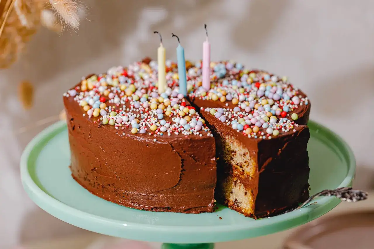 Schokoladen-Geburtstagskuchen mit bunten Streuseln und Kerzen. Ein St&uuml;ck ist herausgeschnitten, das Innere zeigt Marmorkuchen. Ein tolles Geburtstagskuchen Rezept!