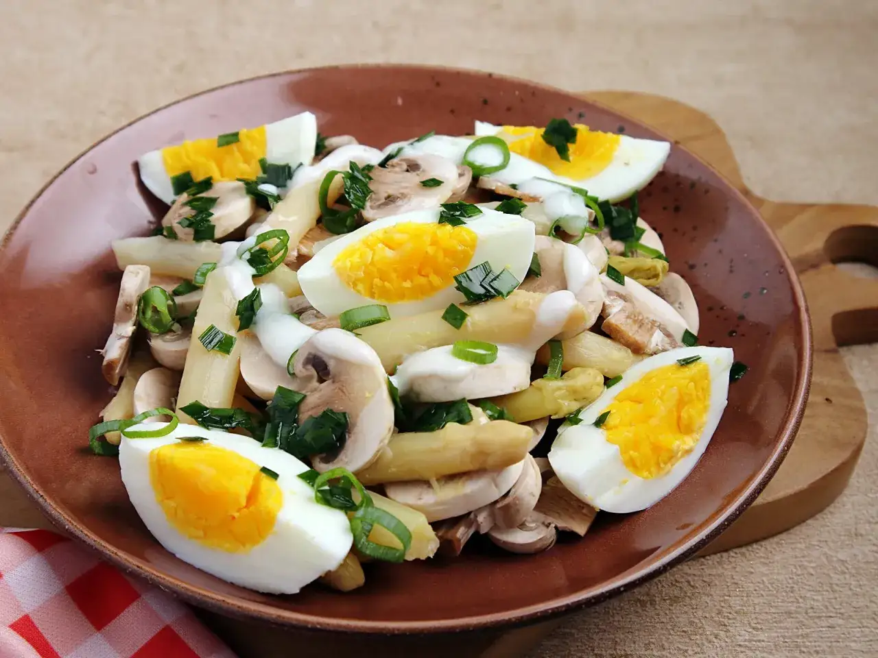 Ein k&ouml;stlicher Spargelsalat mit Ei, Pilzen und Fr&uuml;hlingszwiebeln auf einem braunen Teller.