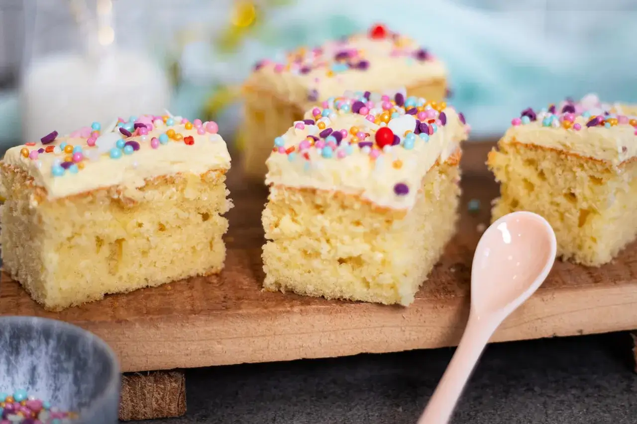 Vier St&uuml;cke saftiger konfetti kuchen mit hellem Zuckerguss und bunten Streuseln, bereit zum Genie&szlig;en.