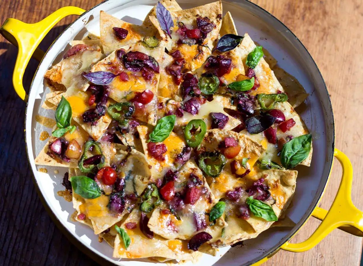 Ein k&ouml;stlicher nacho salat mit geschmolzenem K&auml;se, Jalape&ntilde;os, Oliven und frischem Basilikum, serviert in einer gelben Pfanne.