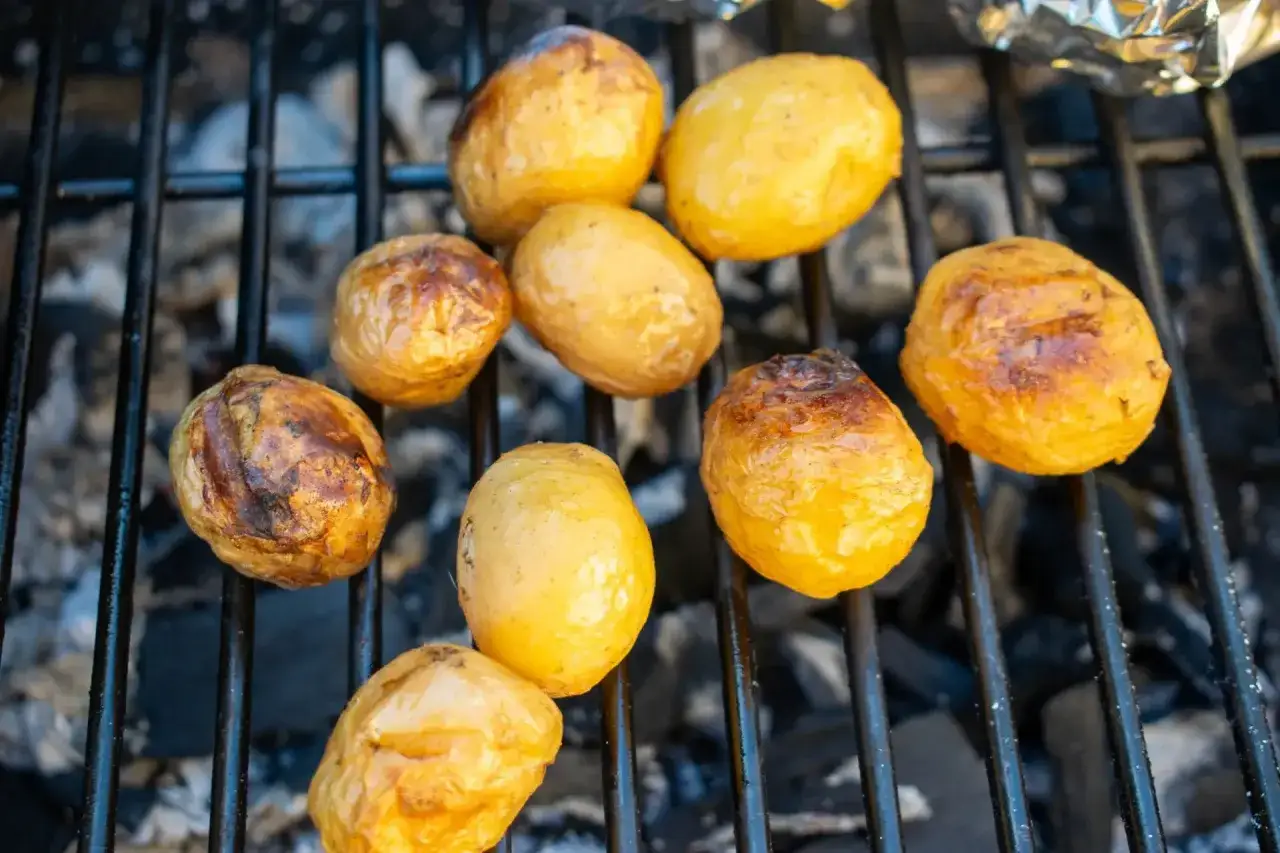 Kleine, goldbraune Kartoffeln garen auf dem Grill. Einige sind leicht angekohlt, andere noch hellgelb. Ein k&ouml;stlicher Anblick!