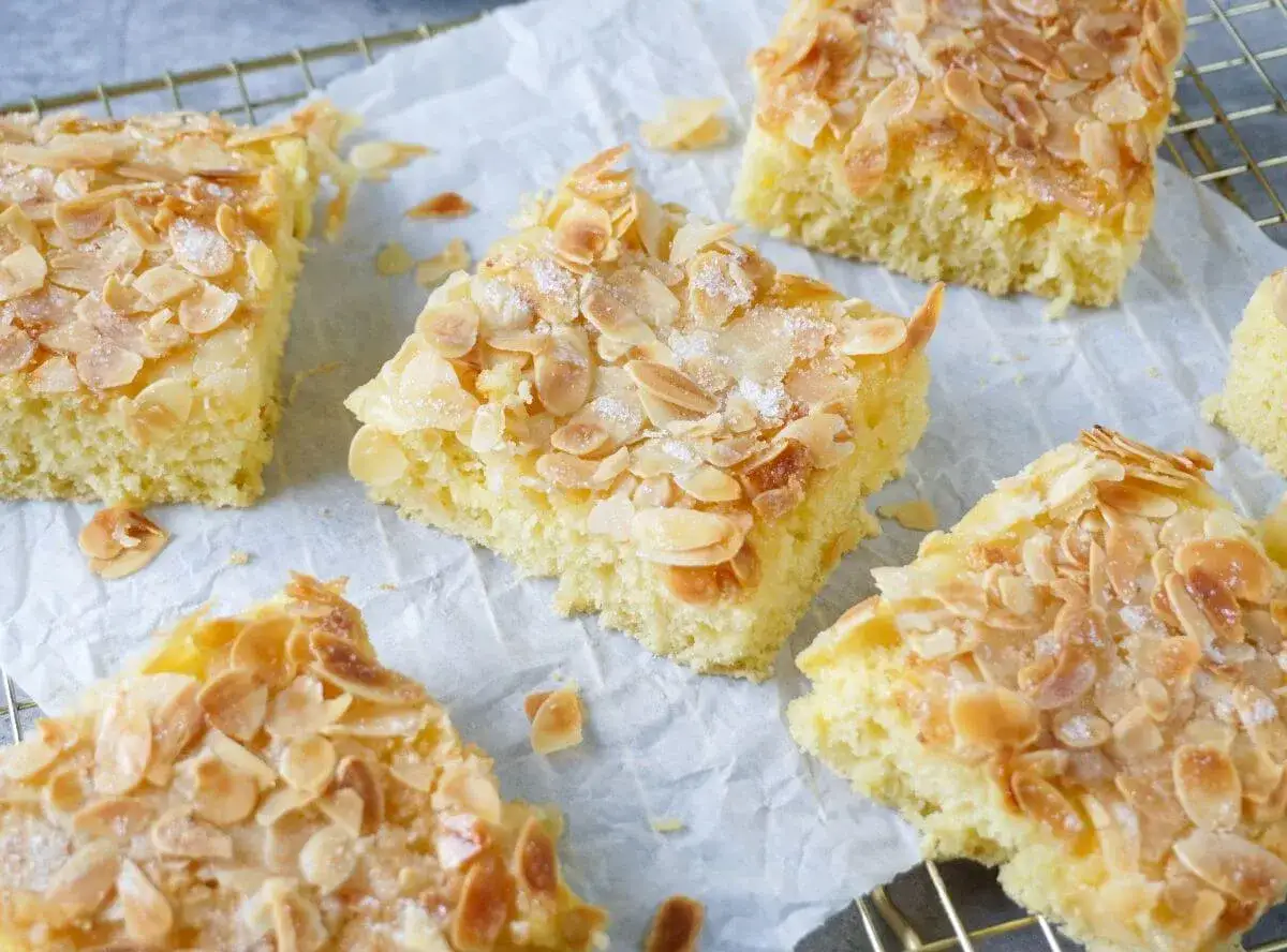 Saftiger Buttermilch Kuchen mit knusprigen Mandelbl&auml;ttchen und Zucker bestreut, auf Backpapier und einem Gitterrost angerichtet.