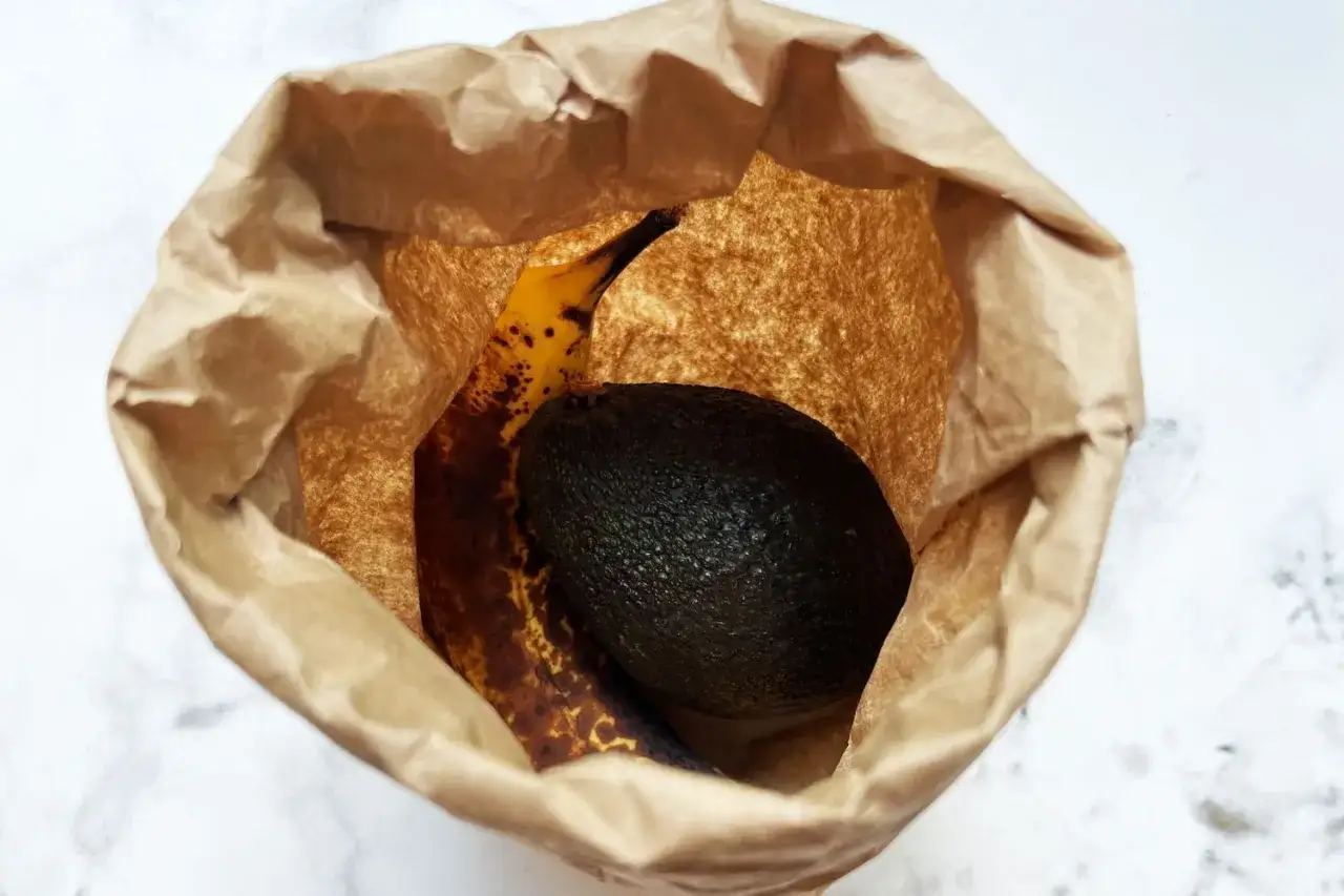 Eine Banane hilft, die Avocado reifen zu lassen. Beide liegen in einer braunen Papiert&uuml;te.