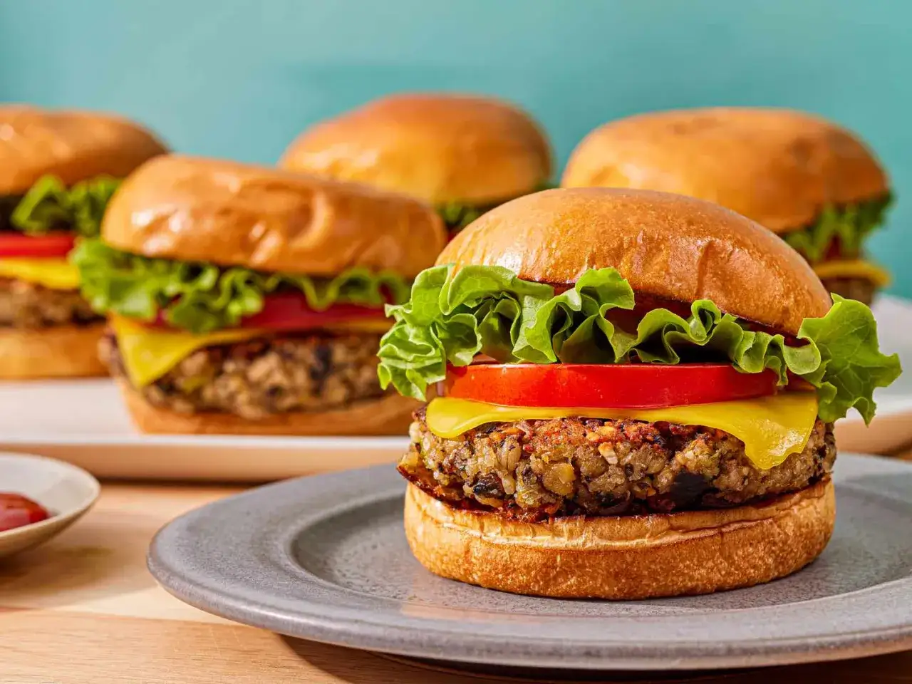 Saftige vegetarische Burger mit Salat, Tomate und K&auml;se auf einem Teller. Im Hintergrund weitere Burger.