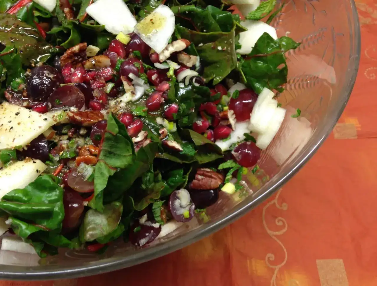 Bunter Salat mit Mangold, Trauben, Granatapfelkernen und N&uuml;ssen in einer Glassch&uuml;ssel.