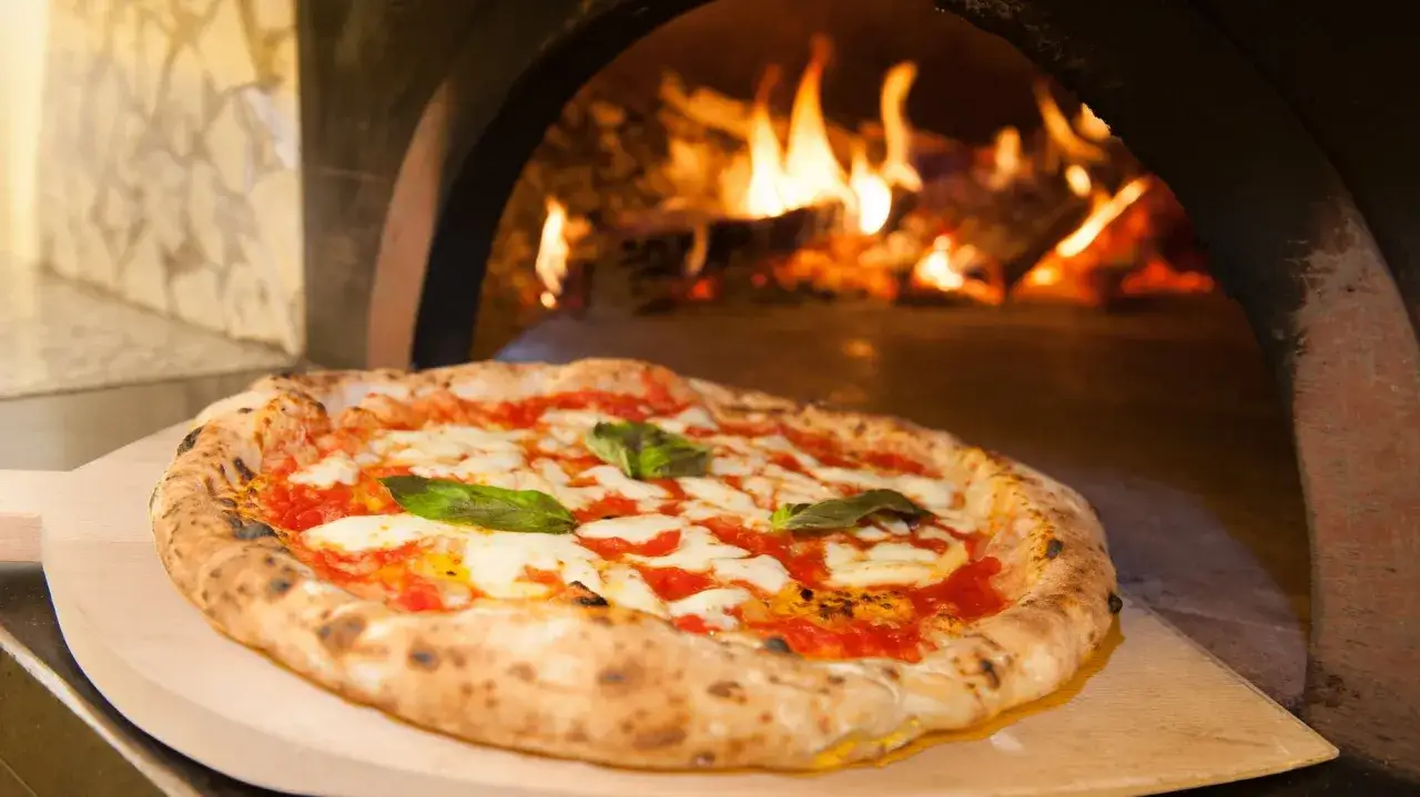 Frisch gebackene Pizza Margherita auf einem Holzschieber, bereit f&uuml;r den Ofen. Das perfekte Pizza Margherita Rezept.