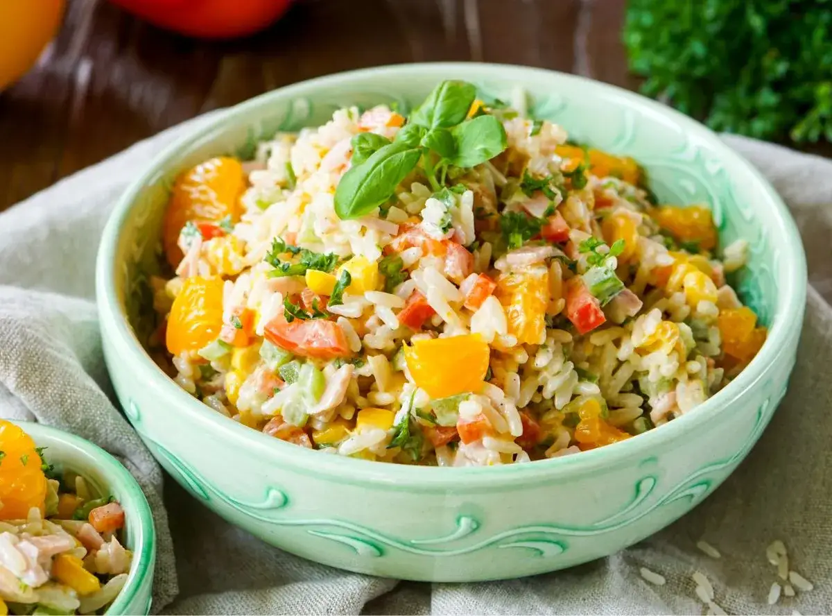 Reissalat mit Mandarinen, Paprika und Kr&auml;utern in einer gr&uuml;nen Sch&uuml;ssel, garniert mit Basilikum.