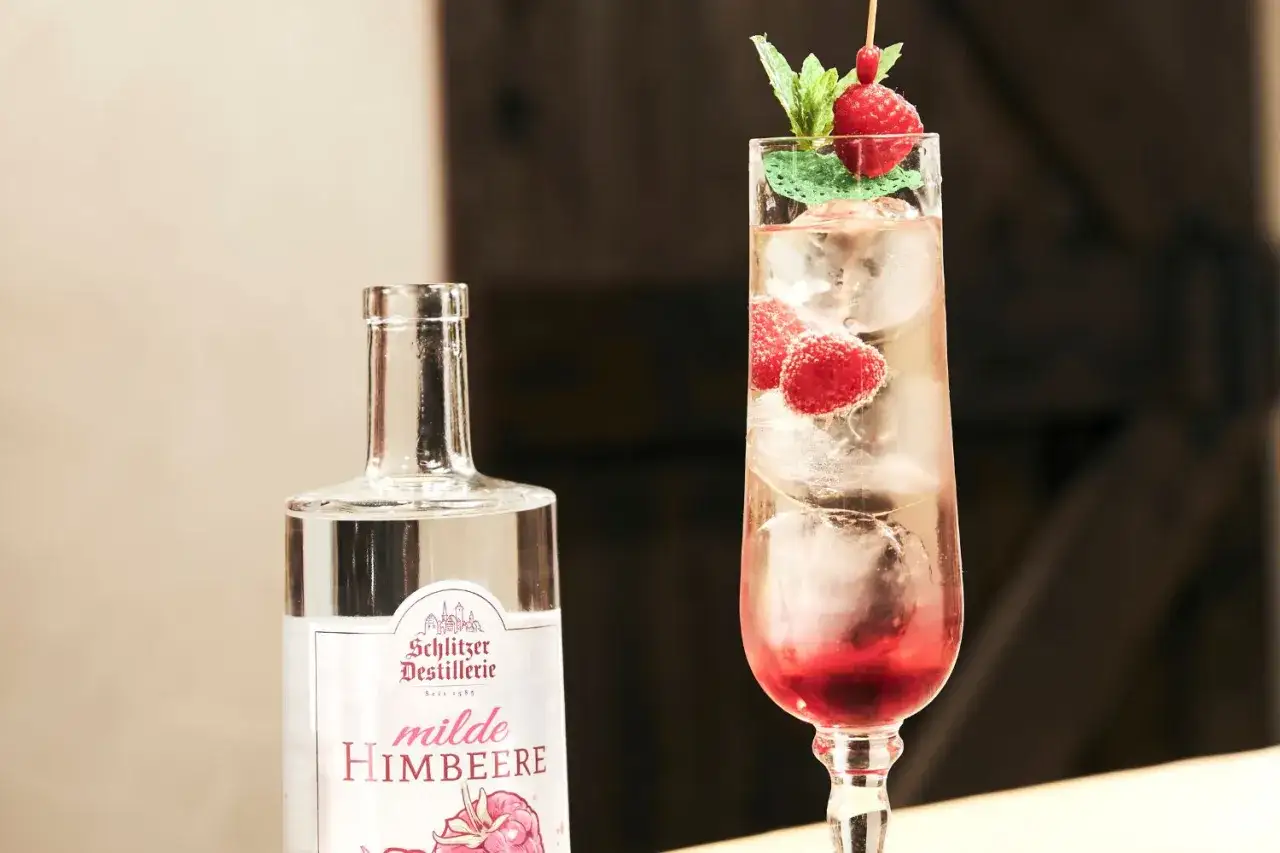 Erfrischender rosato spritz mit Himbeeren und Minze, daneben eine Flasche 