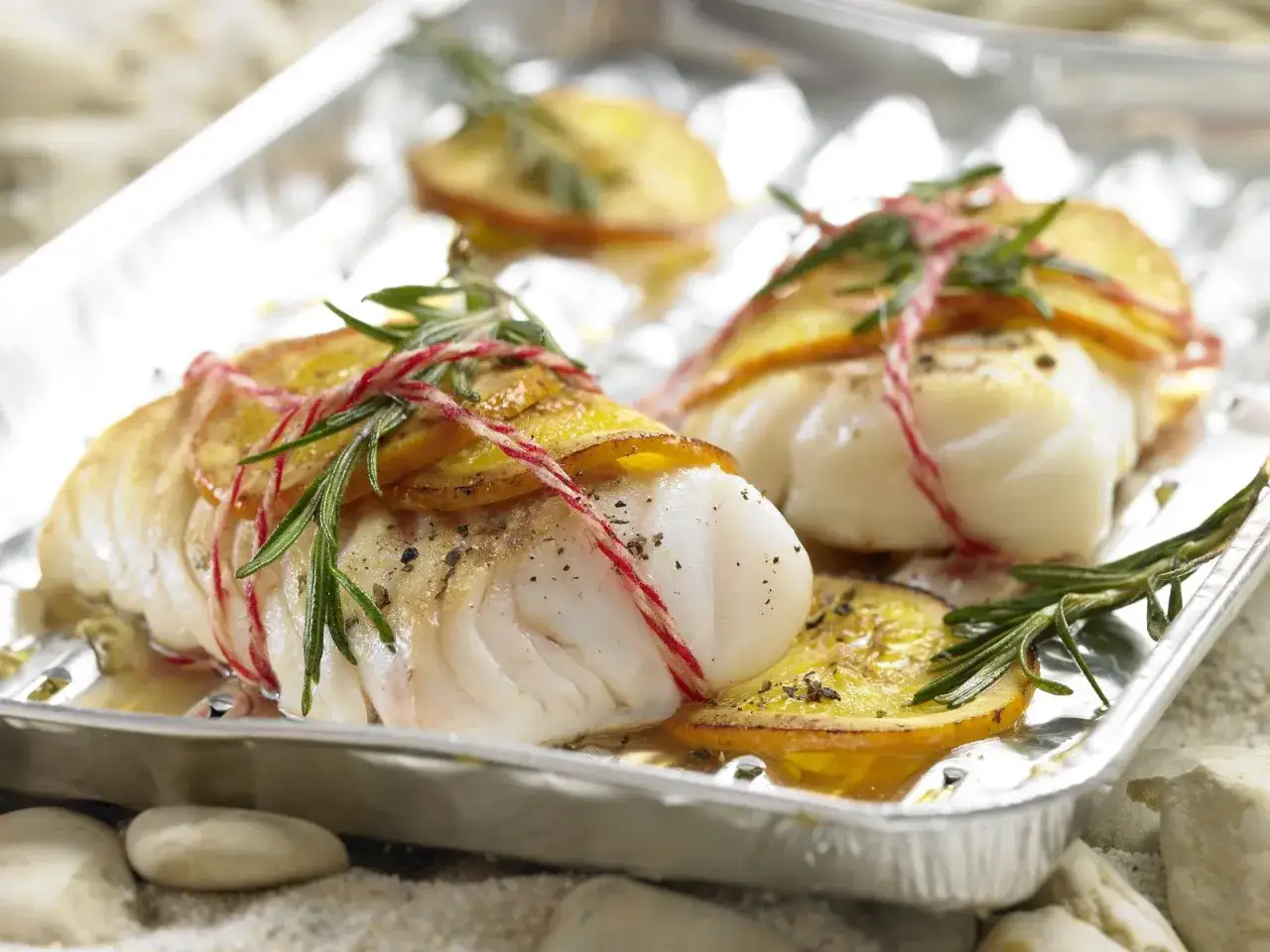 Zwei Filets Kabeljau, mit Zitronenscheiben und Rosmarin umwickelt, werden auf einem Blech gegrillt. Ein k&ouml;stliches Gericht, kabeljau grillen ohne alufolie.