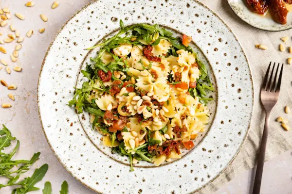 Ein köstlicher mediterraner Salat mit Farfalle, getrockneten Tomaten, Rucola und Pinienkernen.